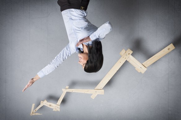 Concept: Successful business trend. Happy talented businesswoman pointing arm upwards in front of ascending business graph, isolated on grey background.